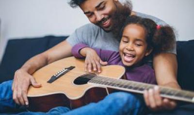 Father and daughter playing a guitar on the couch